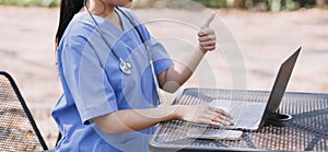 Female Doctor Wearing Scrubs In Hospital Corridor Using Digital Tablet