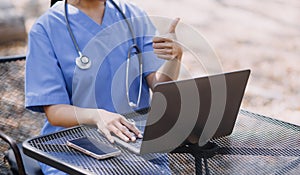 Female Doctor Wearing Scrubs In Hospital Corridor Using Digital Tablet