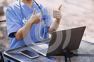 Female Doctor Wearing Scrubs In Hospital Corridor Using Digital Tablet