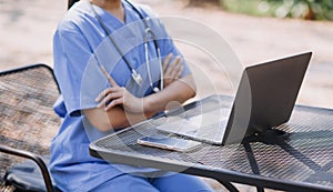 Female Doctor Wearing Scrubs In Hospital Corridor Using Digital Tablet