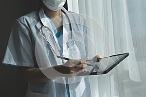 Female Doctor Wearing Scrubs In Hospital Corridor Using Digital Tablet