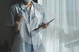 Female Doctor Wearing Scrubs In Hospital Corridor Using Digital Tablet