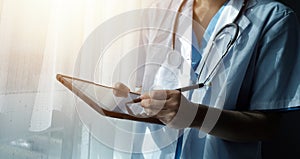 Female Doctor Wearing Scrubs In Hospital Corridor Using Digital Tablet