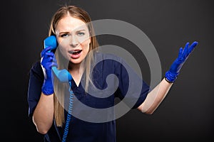 Female doctor wearing scrubs yelling at telephone receiver