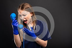 Female doctor wearing scrubs yelling at telephone receiver