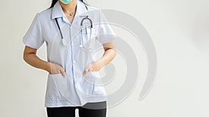 Female doctor wearing a stethoscope on her neck and put her hands in her pocket, white wall background