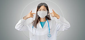 Female doctor wearing stethoscope and protective mask points her fingers to the mask calling for protect yourself