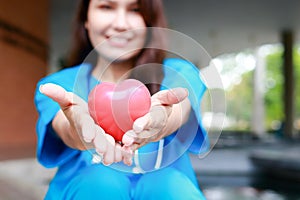 Female doctor wearing a surgical gown holding a heart-shaped ball Put your hand out in front of you