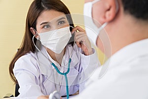 The female doctor wearing a surgical mask and using a stethoscope to check the pulse and look at a male patient
