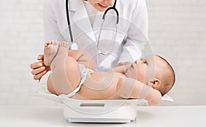 Female doctor weighting cute baby in clinic