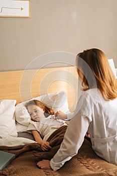 Female doctor in white coat listening to heartbeat with stethoscope to check up little sick girl lying in bed at