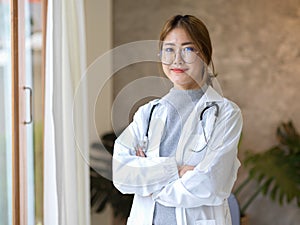 Female doctor in white coat standing in her clinic with crossed arms