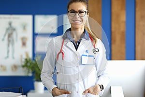 Female doctor in white coat stands in medical office.