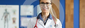 Female doctor in white coat stands in medical office.