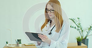 Female doctor in white coat using modern TabletPC device with touch screen. Doctor using DigitalTablet texting to