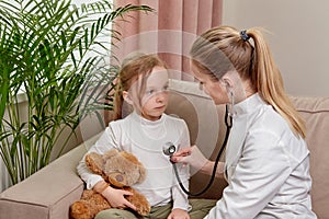 A female doctor in white medical coat is listening to child with a phonendoscope