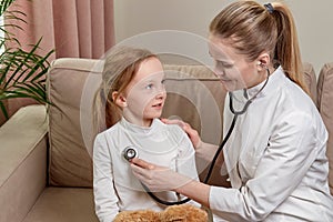 A female doctor in white medical coat is listening to child with a phonendoscope