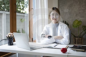 Female doctor in white medical uniform sitting at office desk and smiling at camera.