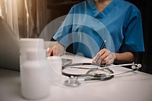 Female doctor working on desk with laptop computer and paperwork in the office.