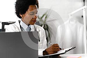 Female doctor working at her office in front of laptop computer, writing a health report