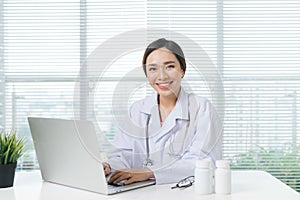 Female doctor working with laptop at office desk and smiling