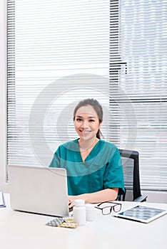 Female doctor working at office desk and smiling at camera, office interior