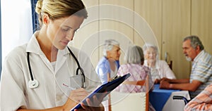 Female doctor writing on clipboard while senior friends interacting in background 4k