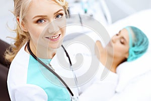 Female doctor and young woman patient in hospital. Physicians examine girl lying at the bed, view from above