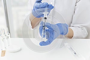 Female doctors hands in blue medical gloves hold syringe and ampoule with vaccine, preparing to make injection.