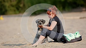 Female dog owner sitting and hugging her dog on the sand on the beach. A woman and her dog spend the weekend together