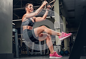 Female doing workouts with trx suspension strips in a gym club.