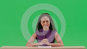 Female in dress sit at the desk isolated on chroma key green screen background. African american woman tv news host