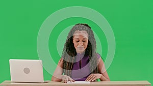 Female in dress sit at the desk isolated on chroma key green screen background. African american woman tv news host sits