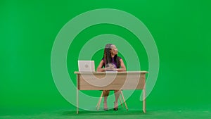 Female in dress sit at the desk isolated on chroma key green screen background. Full shot african american woman tv news
