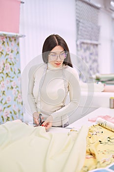 Female dressmaker cuts fabrics with professional scissors