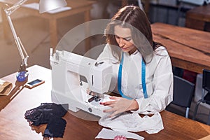 Female dressmaker working with sewing machine, stitching fabric sitting at table in studio