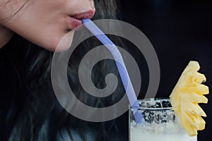 Female drinking pineapple cocktail. Piece of fruit and straw, a close-up mouth and a glass.