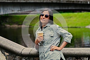 Female drinks coffee on the go in a summer park near the lake.