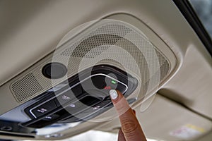 Female driver finger presses the sos button on the ceiling panel of a modern car