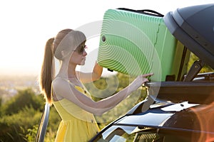Female driver putting green suitcase inside her car roof trunk. Travel and vacations concept
