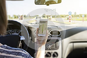 Female driver sitting in the car and holding black mobile smart phone with map gps navigation application with planned