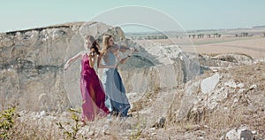 Female duet in elegant blowing dresses plays the violin among picturesque rocks