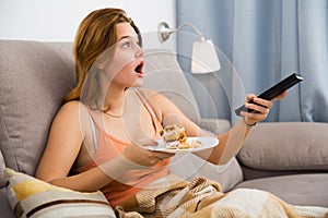 female eating cake at home with tv remote