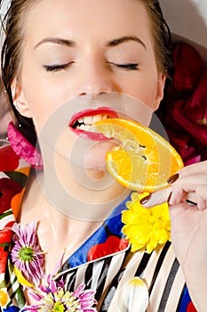 Female eating orange slice over bath background