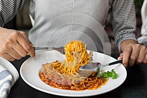Female eating spaghetti with tomato sauce in white plate