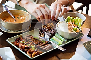 Female eating thai barbecue chicken and beef serviced on the plate in a thai meal photo