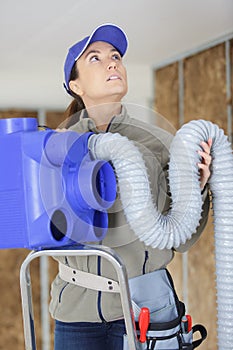 Female elctrician fitting air conditions pipe in building ceiling