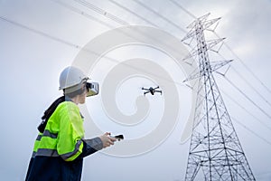 A female electrical engineer flying drone survey area of high voltage pylon with vr goggles at high voltage power plant pylon to