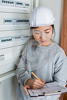 Female electrician with clip-board next to fuse box