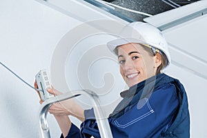 female electrician installing alarm in ceiling